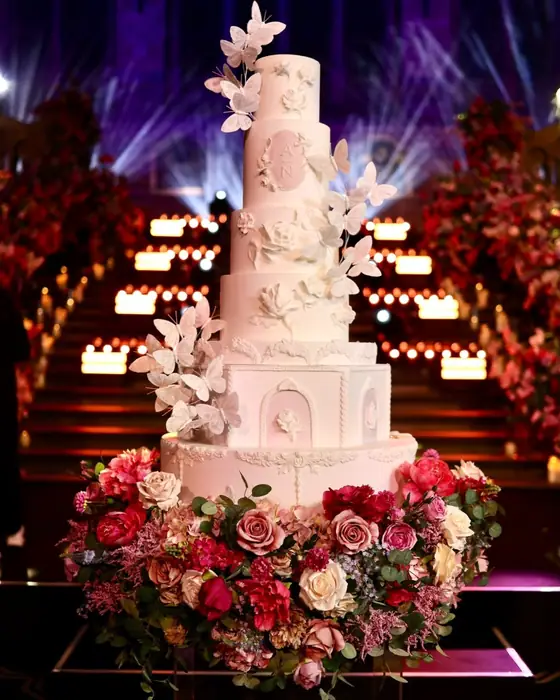 Seven tier blush wedding cake with sugar butterflies and bas relief roses, lit by candles on a staircase