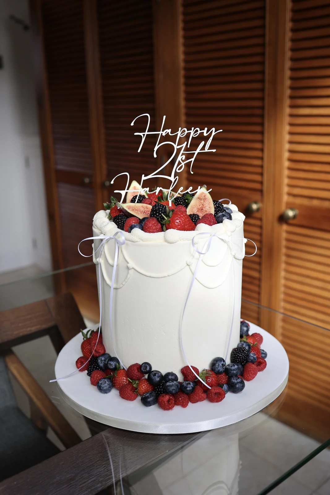 White birthday cake with piped swags, ribbon bows, fresh berries and a birthday topper.