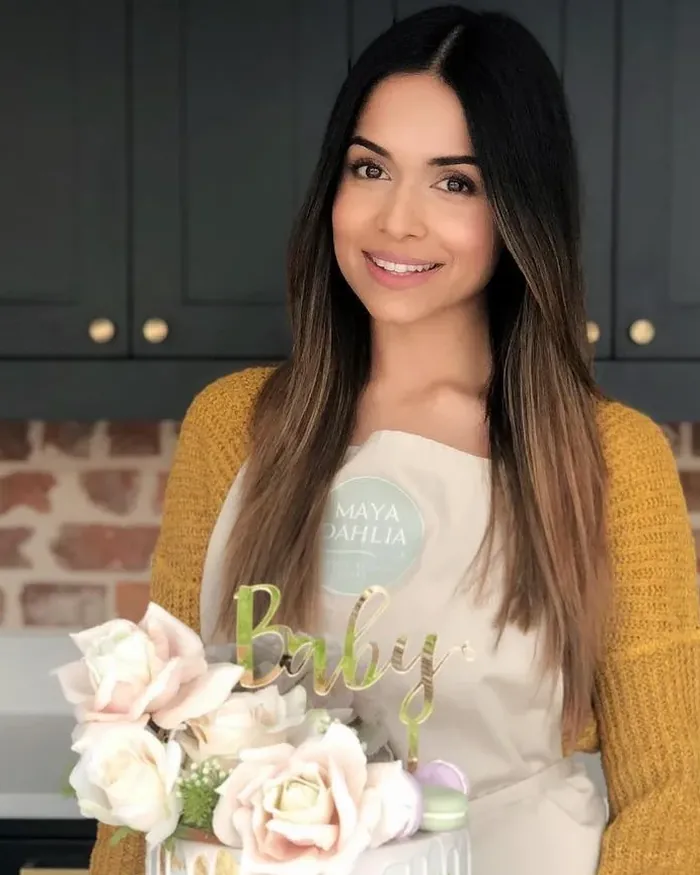 Krishma in a Maya Dahlia apron holding a finished cake dressed with sugar roses
