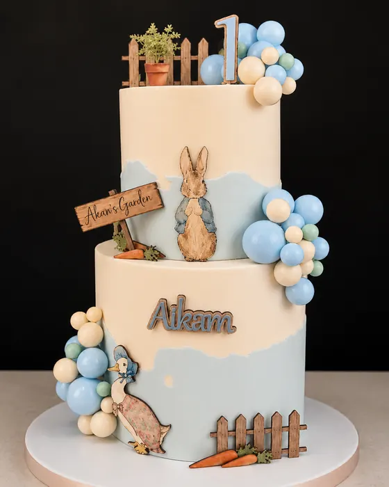 The finished two tier first birthday cake with hand painted Peter Rabbit and Jemima Puddle-Duck, a sugar balloon garland and the name Aikam